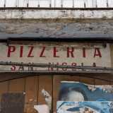 L�insegna � disposta su un vecchio portone in legno marrone sul quale sono stati attaccati negli anni numerosi volantini pubblicitari. � evidente lo stato di abbandono del posto che � stato attivo dal 1980 al 1990
